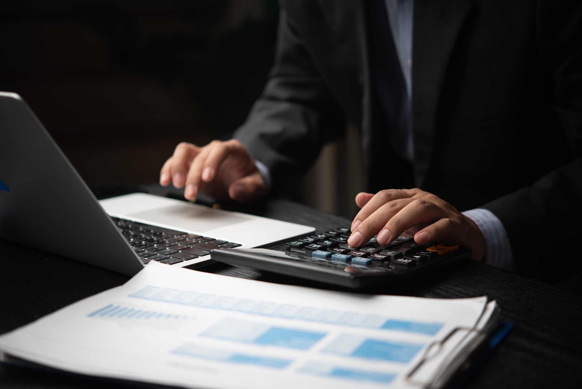 A businessman is using a calculator and laptop to analyze financial reports and data for business budgeting or planning bookkeeping payroll and budget tax. document finance accounting investment